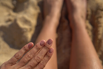 Nude brown natural summer manicure on the hands of a girl on the beach against a background of sand