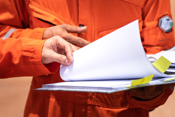 A worker in orange coverall uniform is opening documents to make a discussion on working procedure,...