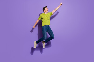 Fototapeta na wymiar Photo of charming strong young man guy wear green t-shirt jumping high smiling isolated violet color background