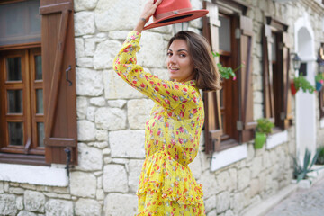 A beautiful young woman with a hat in a dress on a cute cozy Turkish street is having fun walking, spinning, posing, smiling