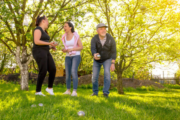 Glad, positive smiling family playing French traditional game petanque in the garden outside during lovely summer day, enjoying leisure time 