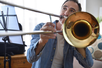 Detail of trombonist practicing trombone in living room at home