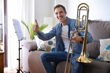 Happy man learning to play trombone at home ok sign
