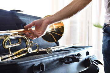 Musician picking up trombone mounted on suitcase in a room