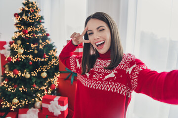 Photo of young cheerful girl blogger take selfie fooling show peace v-symbol decor christmas tree indoors