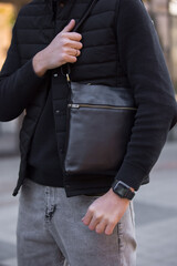 Closeup unrecognizable man holding black leather messenger bag in a city