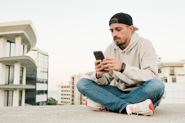 Young handsome man using phone on the street. Sitting with smartphone.