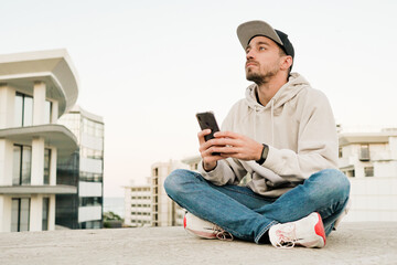 Young handsome man using phone on the street. Sitting with smartphone.