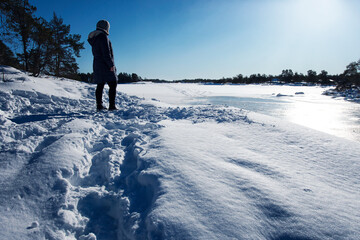Fototapeta na wymiar Woman walking in the snow, looking out over the winter landscape and frozen water on a sunny day in the archipelago in Sweden.