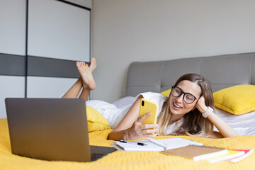 Telecommuting in quarantine. Woman using laptop on bed. Stylish young freelancer working from home....