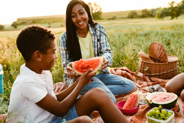 Black family eating watermelon during picnic on summer field