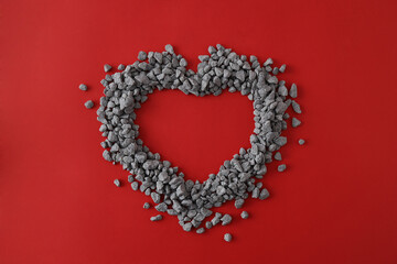 Top view of shape of heart made out of little pebbles on red background