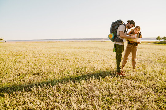 White couple with backpacks examining map while hiking together outdoors