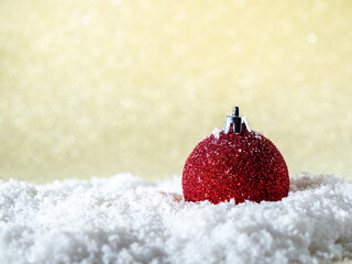Red Christmas ball in the snow on a background of golden glitter.