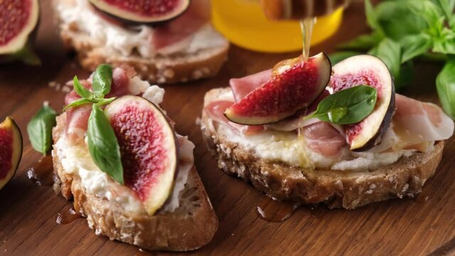 Bruschetta with figs, prosciutto and ricotta cheese. Pouring honey on savory appetizer bruschetta