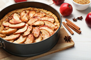 Delicious apple pie and ingredients on white wooden table