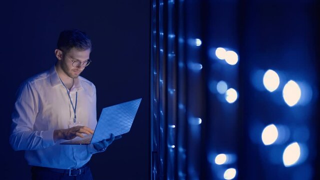 Male Server Engineer in Data Center. IT engineer inspecting a secure server cabinet using modern technology laptop coworking in data center.