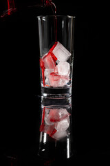 Pouring red non alcoholic solution on the top of the ice into the glass against complete dark background. Pour alcohol,