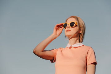 Style woman in pink dress with yellow glasses on blue sky background