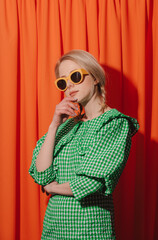 Style woman in green dress and sunglasses on orange curtains as background