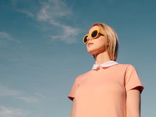 Style woman in pink dress with yellow glasses on blue sky background