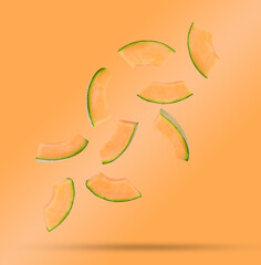 Flying fresh cantaloupe melon slices isolated on orange background.