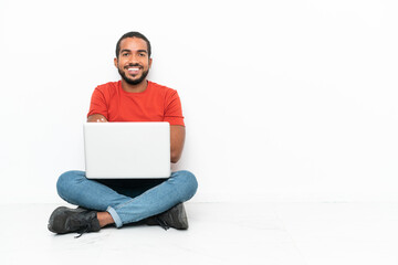 Young Ecuadorian man with a laptop sitting on the floor isolated on white background keeping the arms crossed in frontal position
