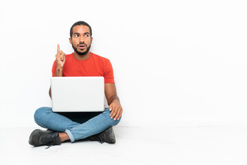 Young Ecuadorian man with a laptop sitting on the floor isolated on white background thinking an idea pointing the finger up