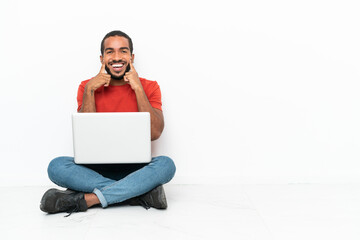 Young Ecuadorian man with a laptop sitting on the floor isolated on white background smiling with a happy and pleasant expression