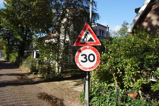 Old road signs in a street in a Dutch village. Work in progress warning sign. Prohibition sign speed limit 30 km per hour. Autumn, October, Netherlands