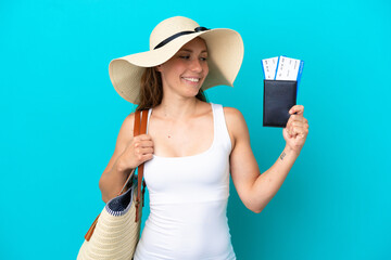 Young caucasian woman holding a beach bag and passport with pamel isolated on blue background with happy expression