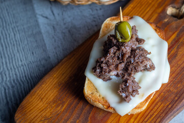 Tostada o tasta de queso con morcilla de cebolla coronada con una aceituna partida verde, pincho o tapa típica de España 