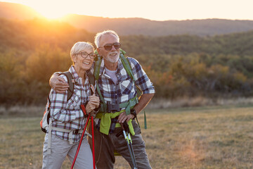 Couple of mature people smile and rest afther walking in nature with sunset on background - obrazy, fototapety, plakaty