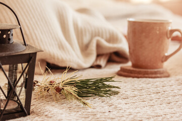 Cozy home atmosphere and decor.  Pine tree branch, a mug with tea or coffee, lantern with a candle, on white knitted background. Winter home still life