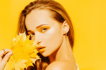 Girl with autumn leaves and red makeup, grimaces and has fun. Autumn photo on a yellow background. Fashion photo model