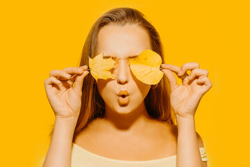 Girl with autumn leaves and red makeup, grimaces and has fun. Autumn photo on yellow background