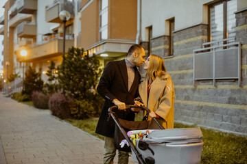 A couple walks with a stroller for a child near houses in the evening for a walk. Children and fresh air. Family, husband and wife in the autumn on the street