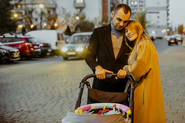 A couple walks with a stroller for a child near houses in the evening for a walk. Children and fresh air. Family, husband and wife in the autumn on the street