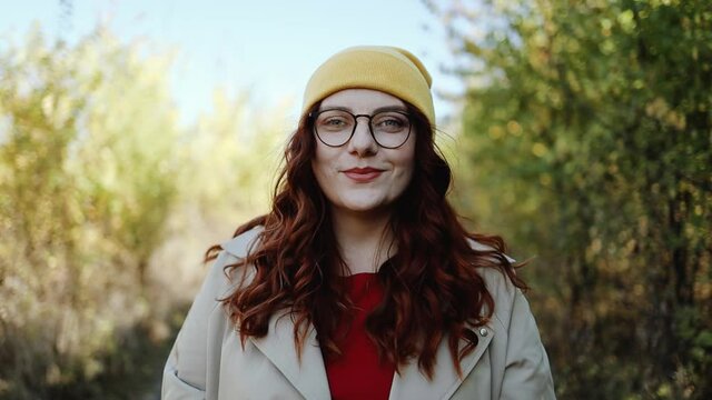 Portrait of happy red-haired curly woman in bright stylish clothes in the park looking on the camera