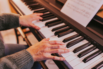 Obraz premium Close-up of girl hands on the piano, woman playing the piano. Christmas lights and music, concert, family time, holidays concept. Merry Christmas, happy new year.