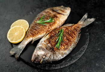 grilled dorado fish with lemon and rosemary on stone background