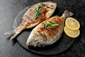 grilled dorado fish with lemon and rosemary on stone background