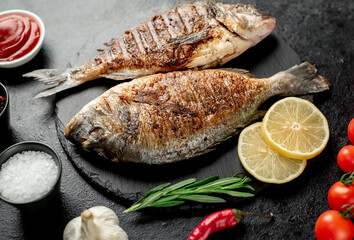 grilled dorado fish with lemon and rosemary on stone background
