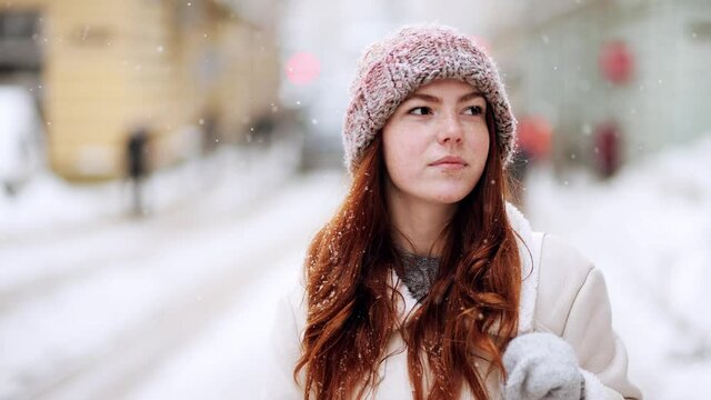 Red haired woman with natural beauty and freckles on her face. Close up portrait of female in snowy holiday city. Snowing outdoors. Winter concept