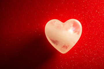 Symbolic photo of transparent stone in shape of a heart on red background. Beautiful amolet for people in love