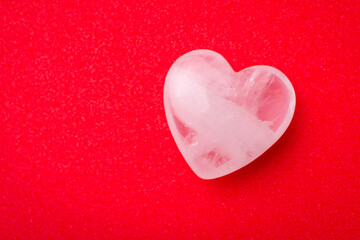 Fototapeta premium White transparent stone in shape of heart on red table. Valentine`s day background