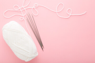 White wool clew and metal needles on light pink table background. Pastel color. Closeup. Knit...