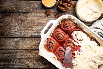 Homemade cinnamon rolls red velvet with cream cheese glaze on wooden background, top view