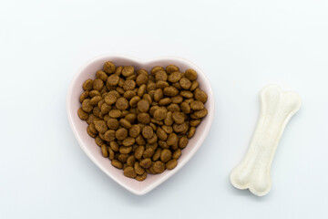 Dog food in a bowl, in the shape of a heart. Two white bones next to a plate