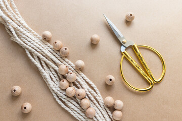 Beige cotton rope for macrame, wooden beads and scissors on craft paper. Handmade and handcraft...